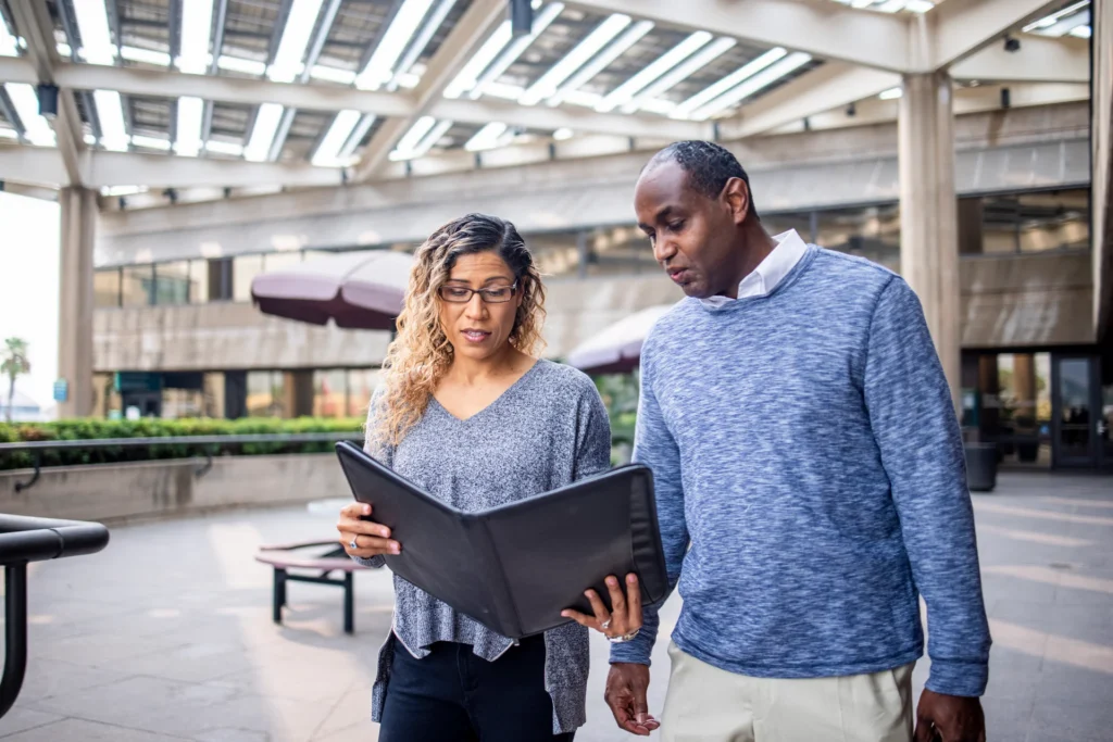 2 people walking in a mall looking at a book